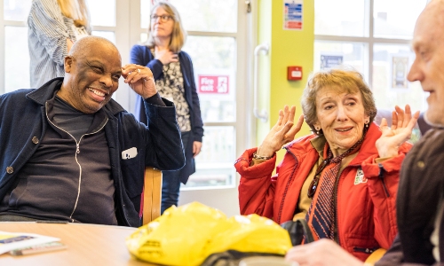 Actor Don Warrington laughs with an older lady and older man at Age UK Barnet