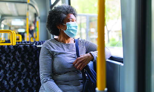 A lady wearing a face mask while sat on a  bus