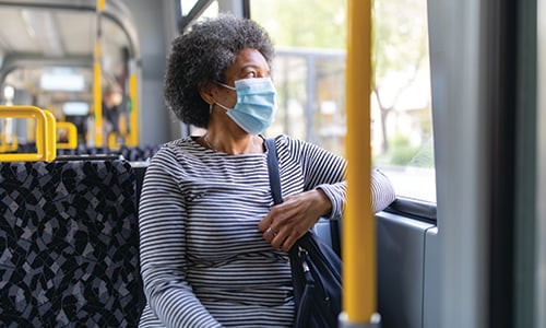 A lady wearing a face mask while sat on a  bus