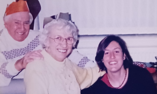 A young dark-haired woman smiles with her grandparents, who are wearing Christmas paper hats