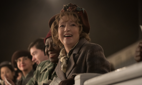 Actress Lesley Manville, dressed in 1950s clothing as lead character Mrs Harris, smiles towards the screen