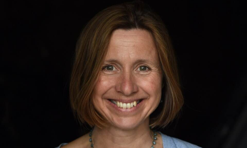 An image of a woman, smiling, photographed against a black background