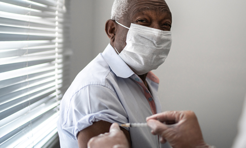 An older man wearing a face mask receives the vaccine