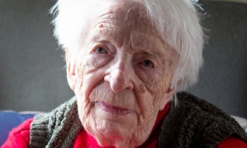 An older woman in a red jumper, looking towards the camera.