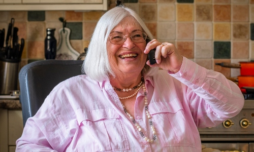 An older lady with glasses and white hair laughs on the phone to a telephone friend