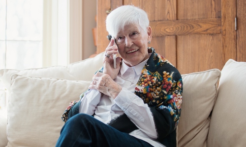 An older lady wearing a shawl sits on a sofa enjoying a phone call