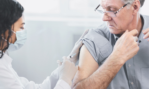 An older man receives a vaccine in his upper arm from a medical professional