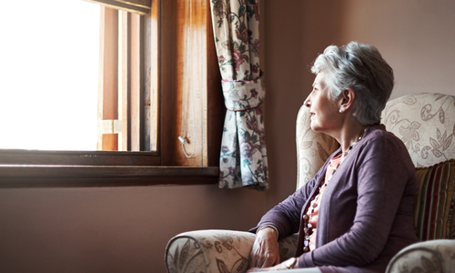 An older woman, sat in chair looking out of the window