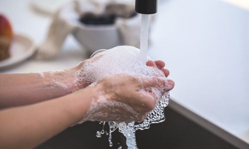 Hands covered in soap under a running tap