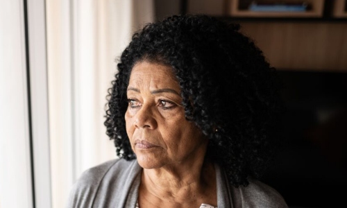 An older Black woman stares thoughtfully out of the window