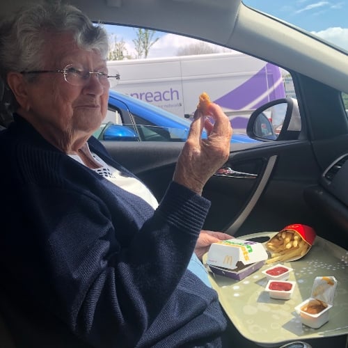 An older lady with glasses eating a McDonalds chicken nugget meal