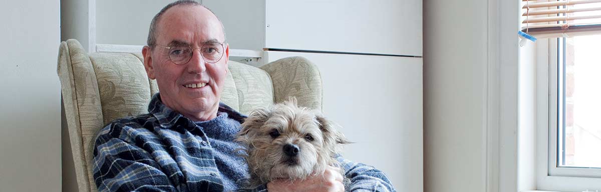 An older man sits with his dog, smiling