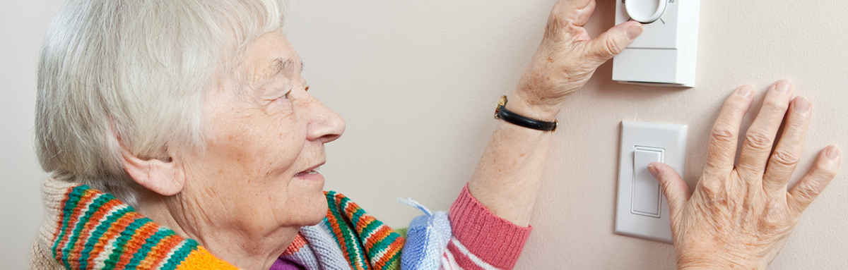 An older woman adjusts a thermostat