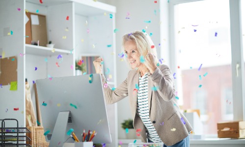 woman at her computer celebrating a lottery win with confetti