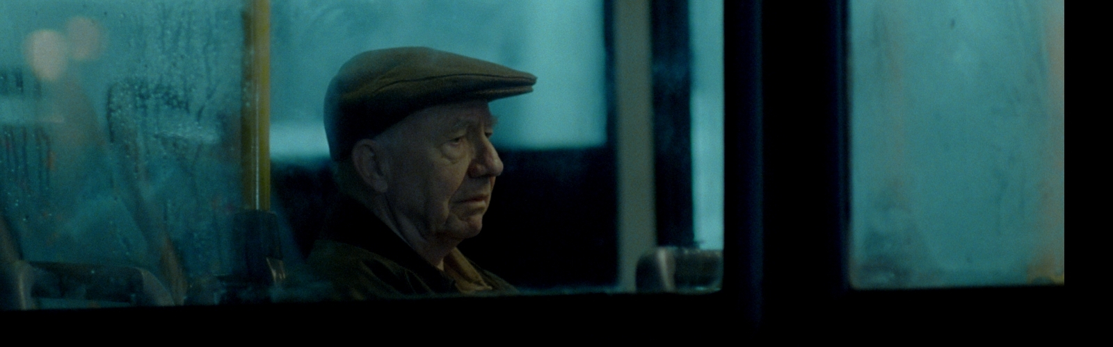 An older man on the phone outside a bus stop, looking concerned