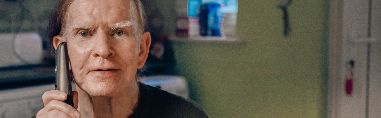 An older man with brown-grey hair on the phone, smiling