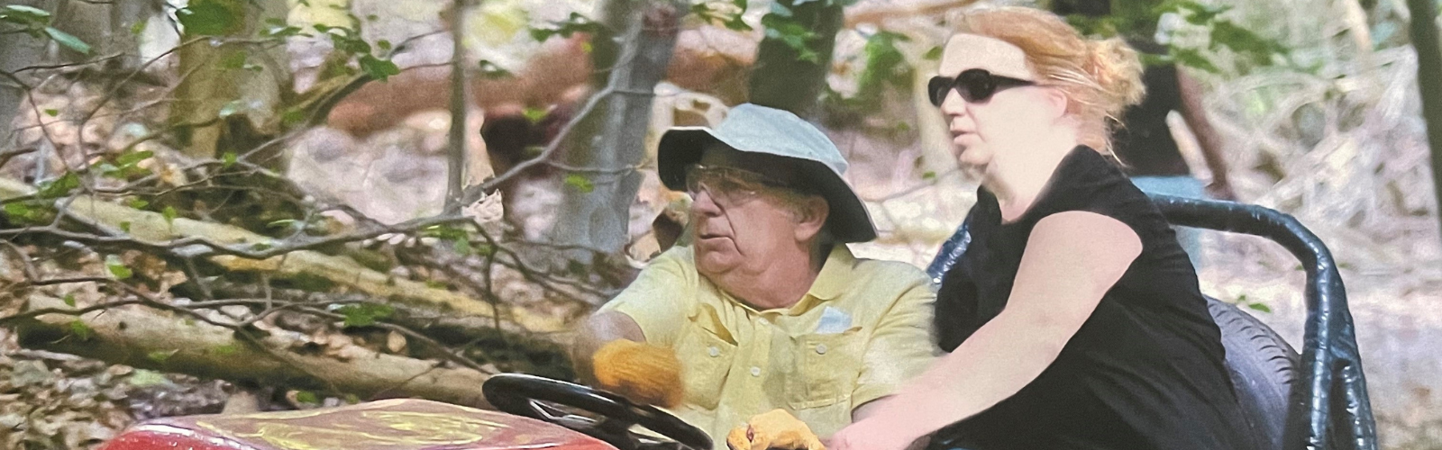 A man and a woman in a motor care, driving through a forested area
