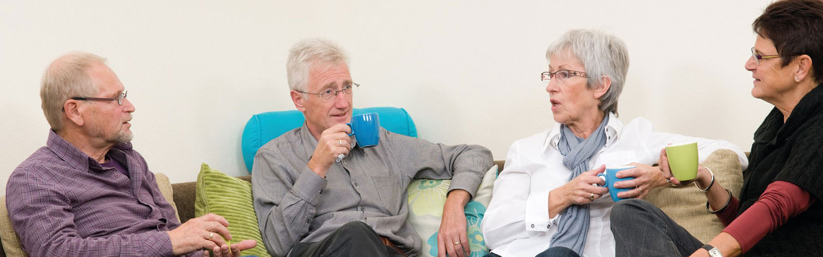 Older people sat in a row on a sofa, drinking tea