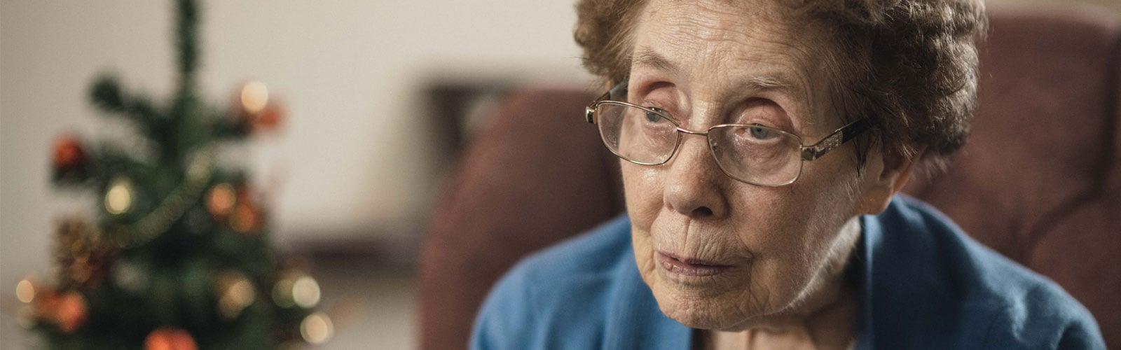 A woman sits sadly by a Christmas tree