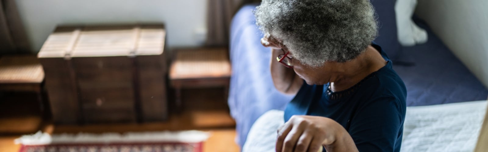 An older woman sits on her bed with her head in her hands