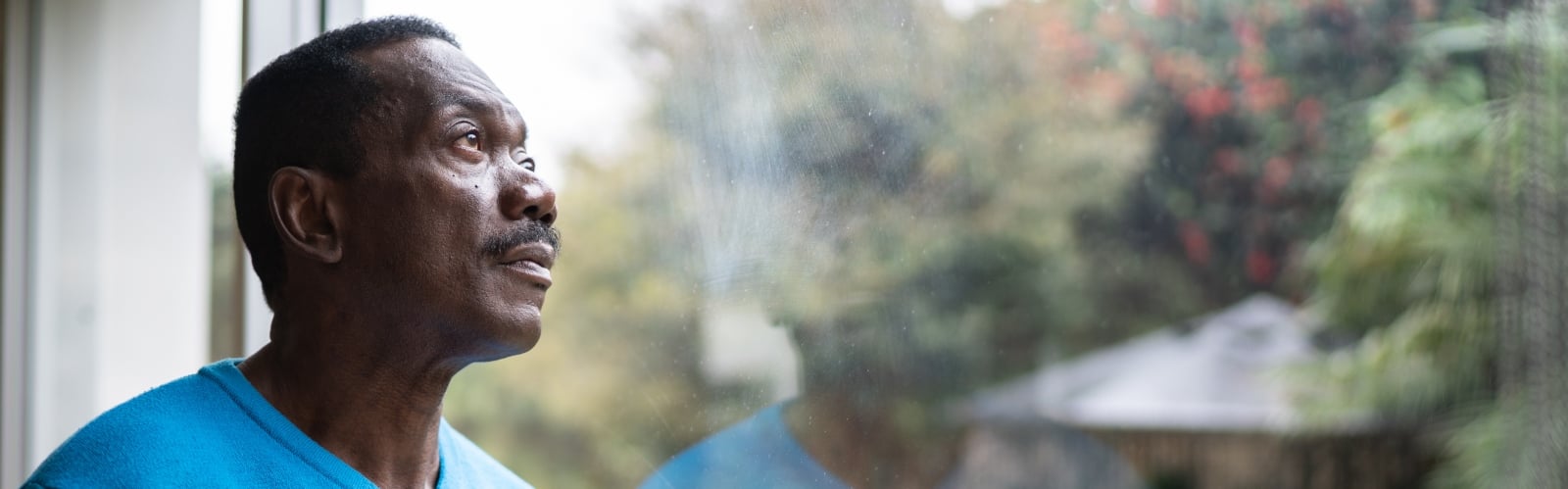 An older Black man stares sadly out of the window