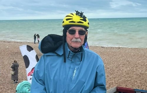 An older man with a grey moustache, dressed in cycling kit at the seaside