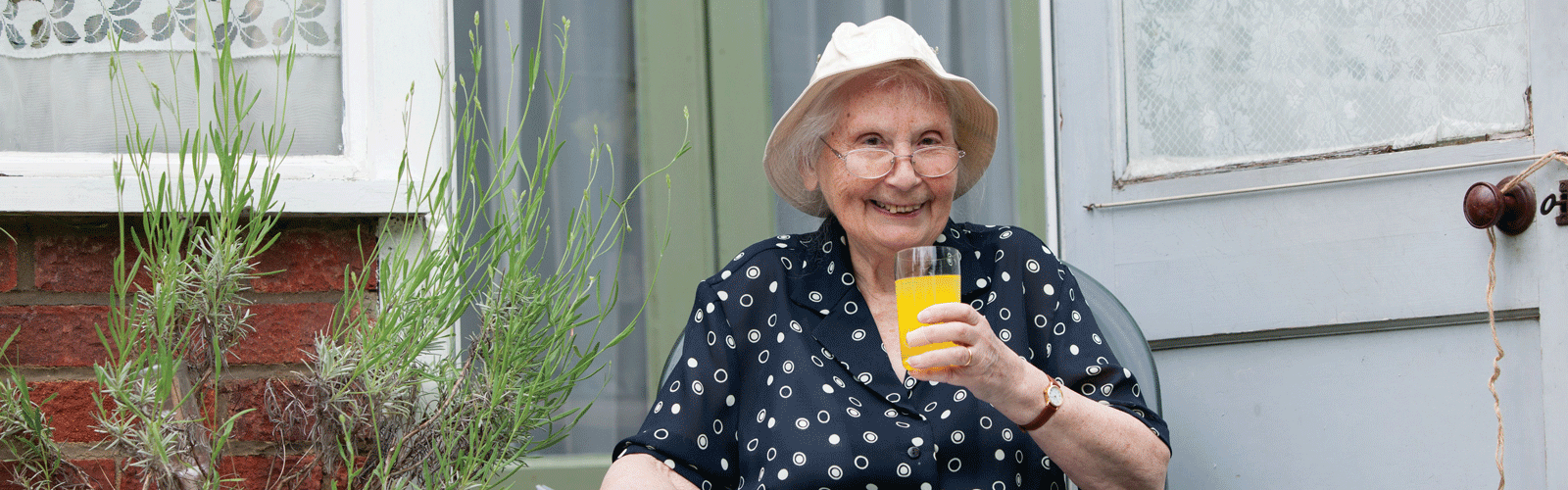 A woman sat in the garden drinking a glass of orange juice. 
