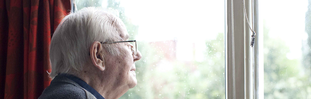An older man, wearing glasses, looking out of the window